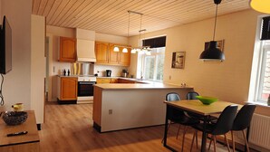 A modern kitchen with wooden cabinets, a central island, and a dining area with chairs.