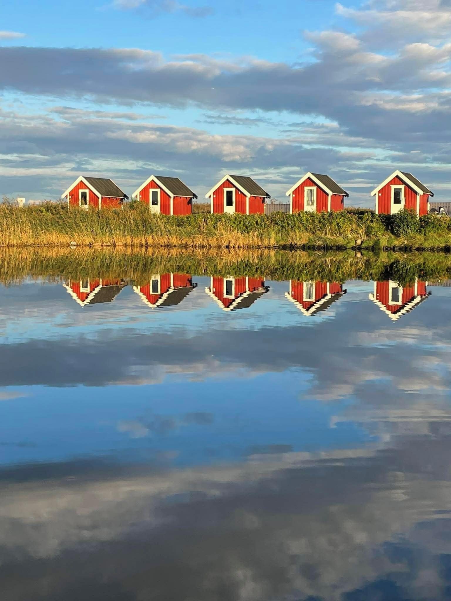 A row of red buildings with a clear reflection in calm water.
