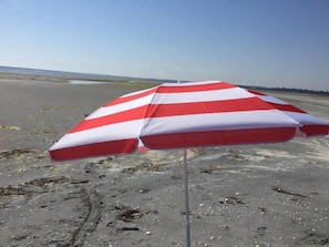 A beach umbrella with red and white stripes on a sandy beach.