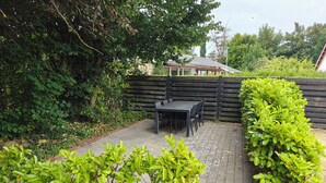 A patio area with a table and chairs, surrounded by greenery and a wooden fence.