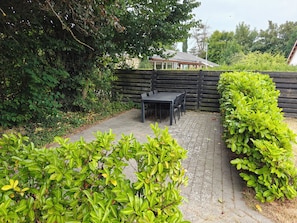Un espace patio aménagé avec une table et des chaises, entouré de verdure et délimité par une clôture en bois.