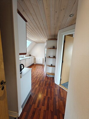 Un pasillo estrecho con suelo de madera, paredes blancas y techo inclinado.