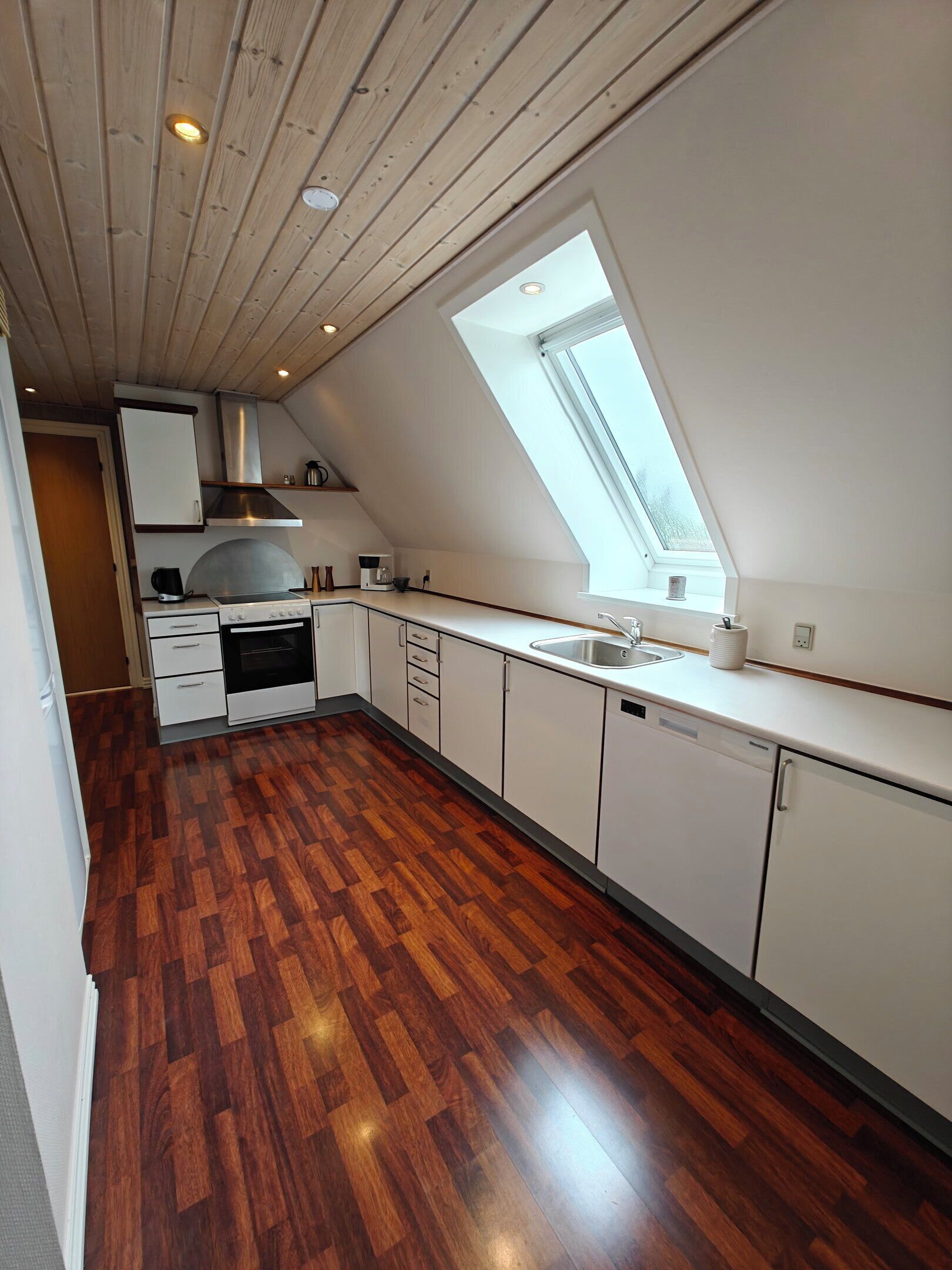 A modern kitchen with a sloped ceiling, wooden flooring, and a skylight.