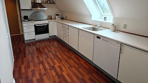 A modern kitchen with a sloped ceiling, wooden flooring, and a skylight.