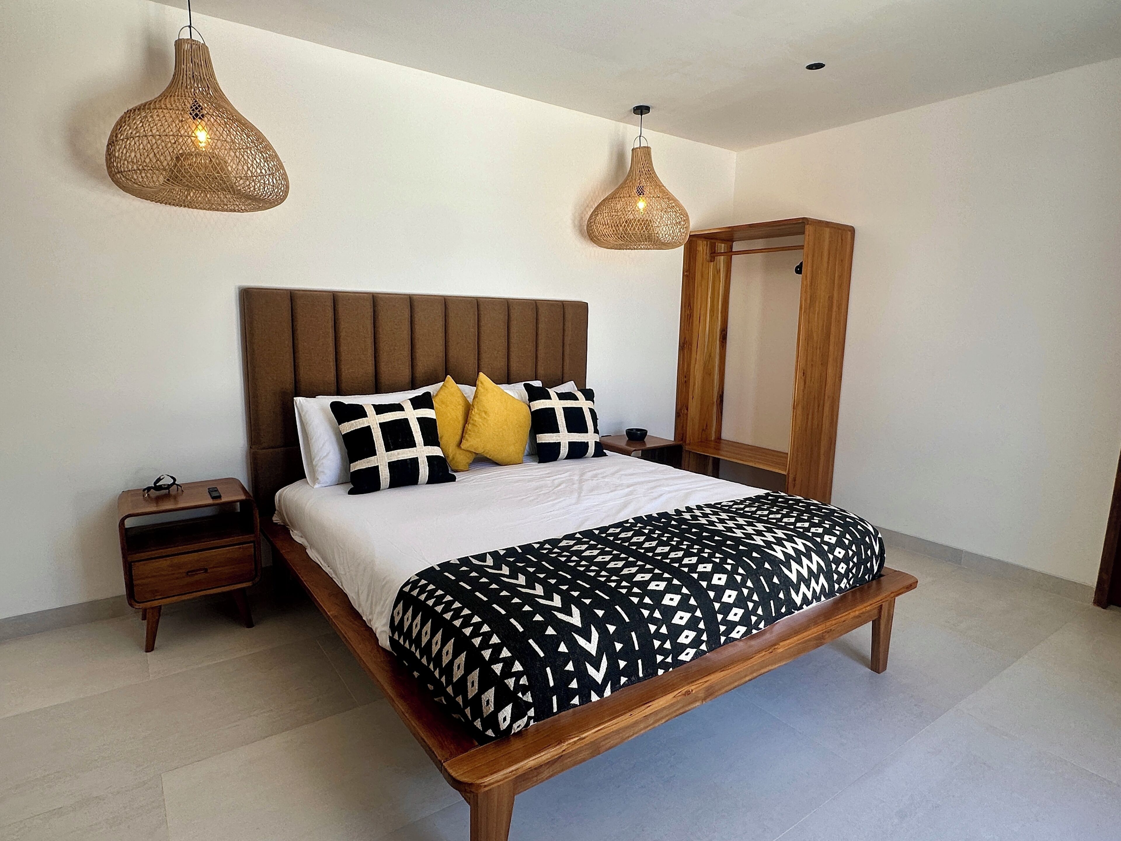 Un lit avec un cadre en bois, une tête de lit et une couvre-lit à motifs. Il y a deux tables de chevet, l’une avec une lampe et l’autre avec un téléphone.