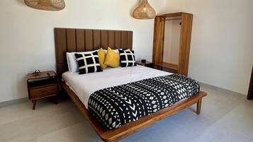 Un lit avec un cadre en bois, une tête de lit et une couvre-lit à motifs. Il y a deux tables de chevet, l’une avec une lampe et l’autre avec un téléphone.