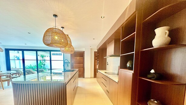 A modern kitchen with a central island, pendant lighting, and built-in shelving.