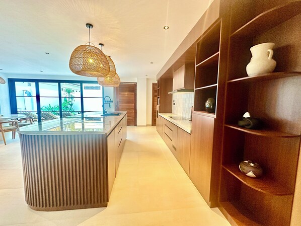 A modern kitchen with a central island, pendant lighting, and built-in shelving.