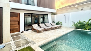 A modern two-story house with a swimming pool, lounge chairs, and a glass door entrance.