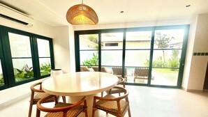 A dining area with a round table and six chairs, large windows, and a view of a garden.