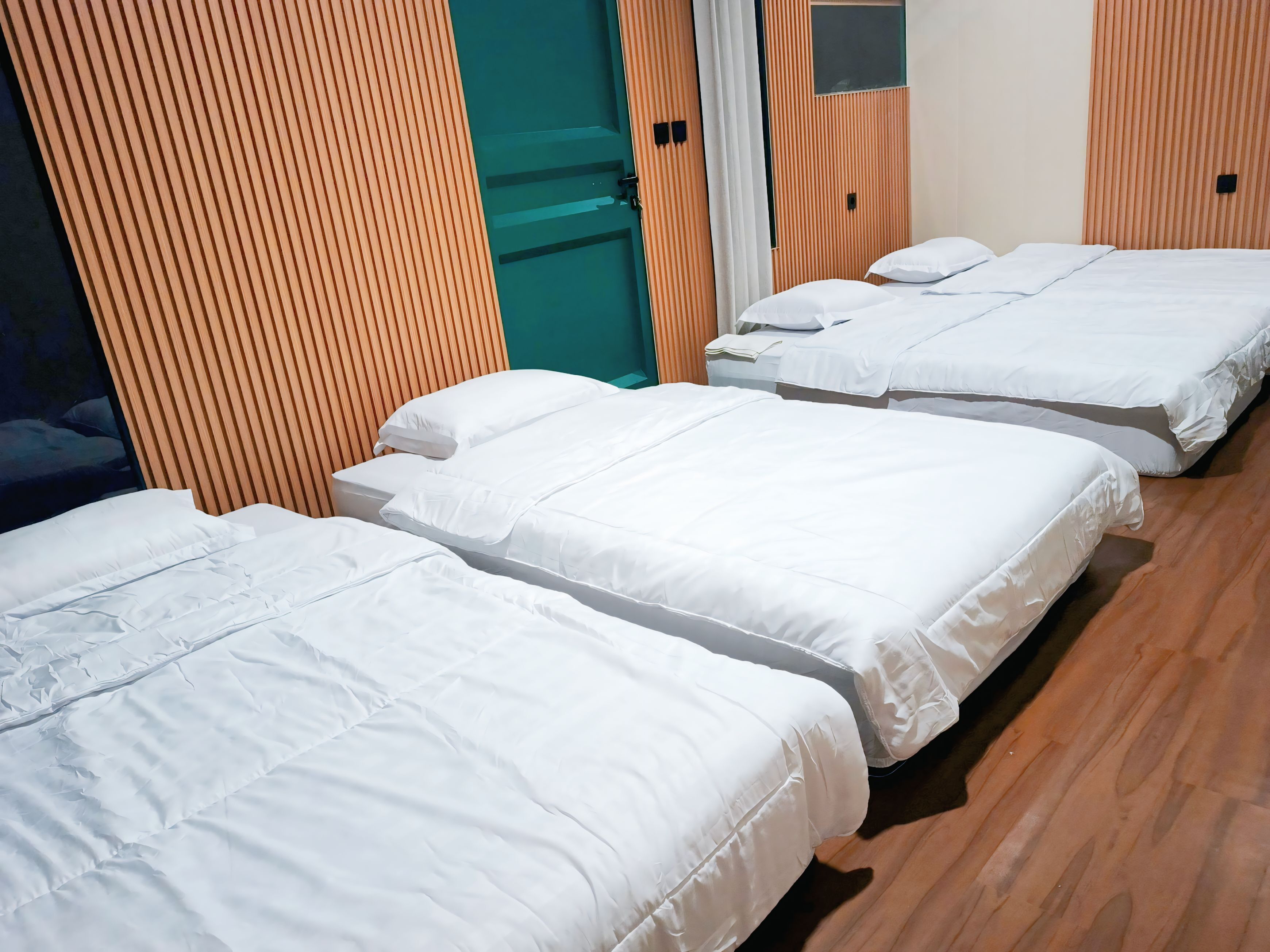 A hotel room with three beds, wooden flooring, and a green door.