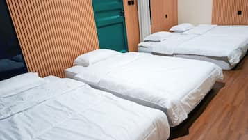 A hotel room with three beds, wooden flooring, and a green door.