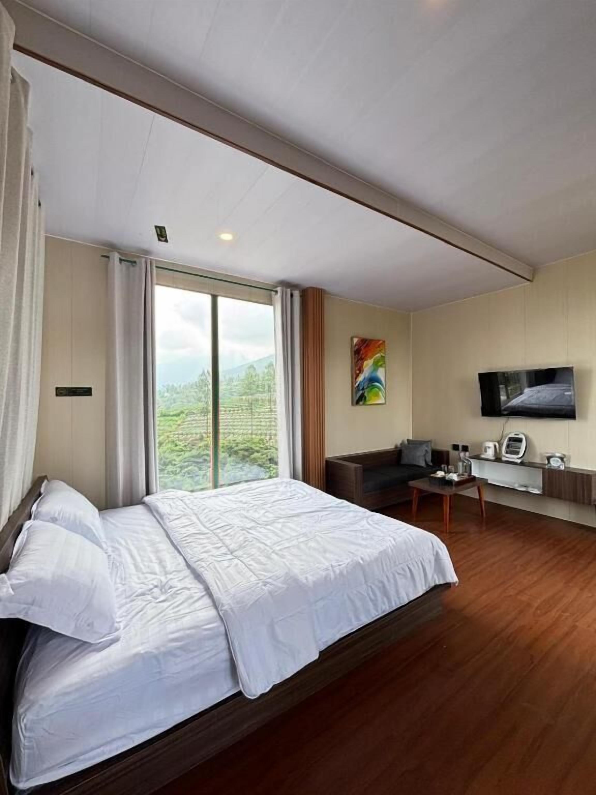 A hotel room with a large bed, a desk, a chair, a television, and a window with a view of greenery.