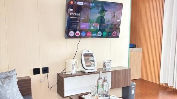 A modern living room with a flat-screen TV mounted on the wall, a coffee table with various items, a sofa, and a wooden cabinet.