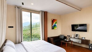 Habitación de hotel con una cama grande, un sofá, un televisor y vistas a un paisaje verde.