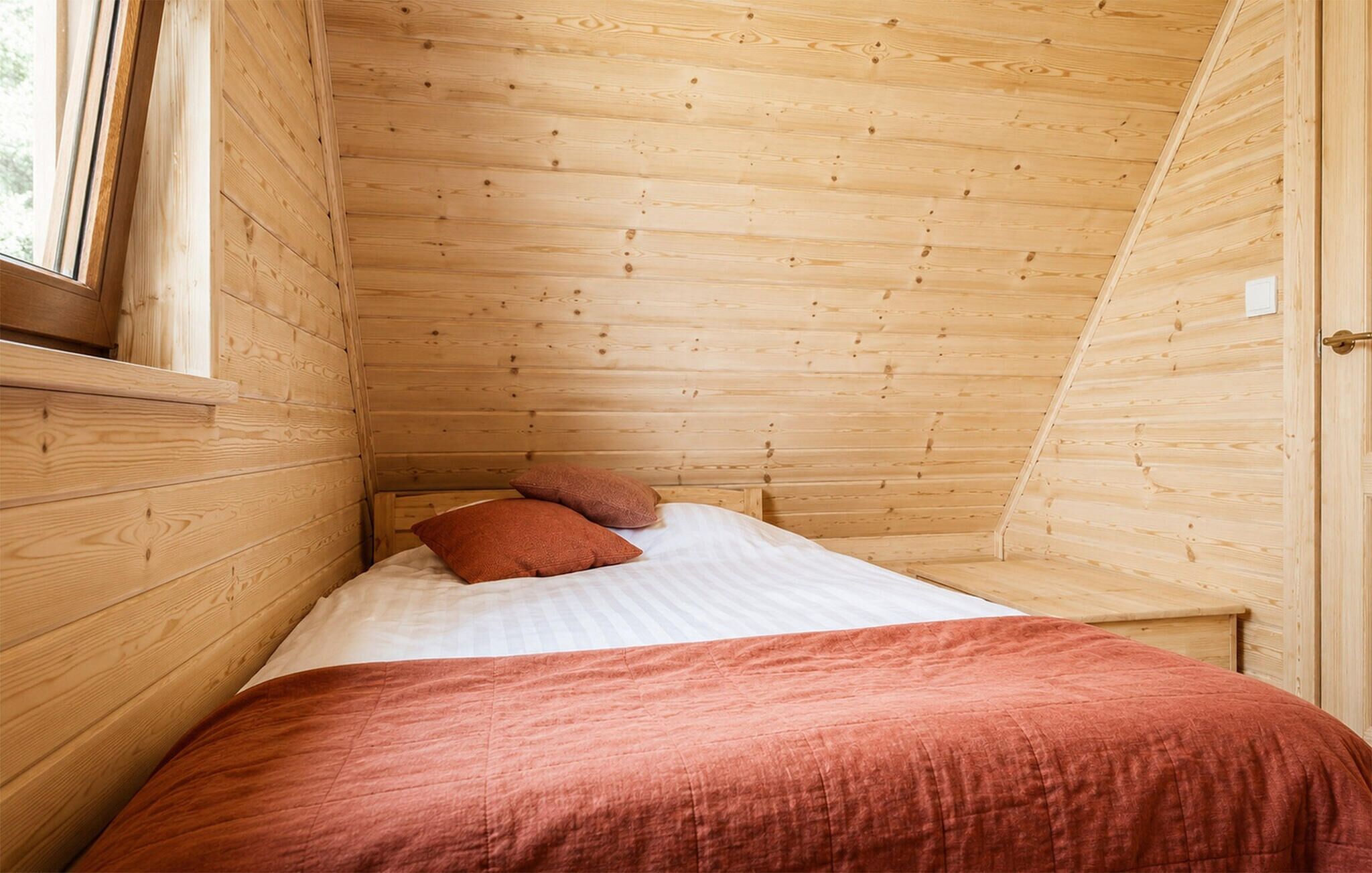 Una habitación pequeña de madera con una cama, almohadas y una ventana.