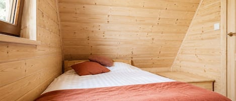Una habitación pequeña de madera con una cama, almohadas y una ventana.