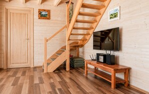 Eine Holztreppe führt zu einem Erkerbereich mit Fernseher und Lautsprechern auf einem Holzbalken.