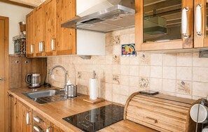 Eine Küche mit Holzschränken, einer Edelstahlspüle, einem eingebauten Ofen und einem modernen Induktionskochfeld.