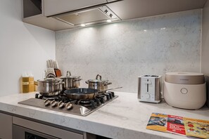 A modern kitchen with a gas stove, pots, a toaster, and a rice cooker. - Zen Sky Home - Super Centre w/ Carpark & Pool (Melbourne)