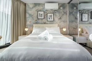A hotel room with a large bed, two bedside tables, a wall-mounted air conditioner, and framed artwork. - Zen Sky Home - Super Centre w/ Carpark & Pool (Melbourne)