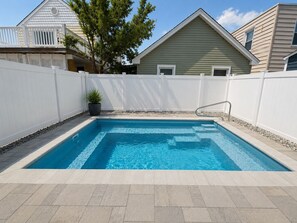Ein rechteckiger Swimmingpool, umgeben von einem weißen Zaun, mit einem Topfpflanze und einem Haus im Hintergrund.