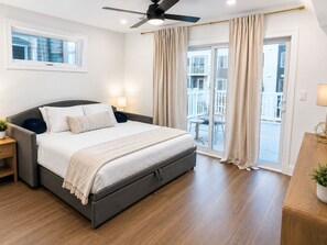 Ein Schlafzimmer mit einem Bett, Nachttischen, einem Deckenventilator und Blick auf einen Balkon.
