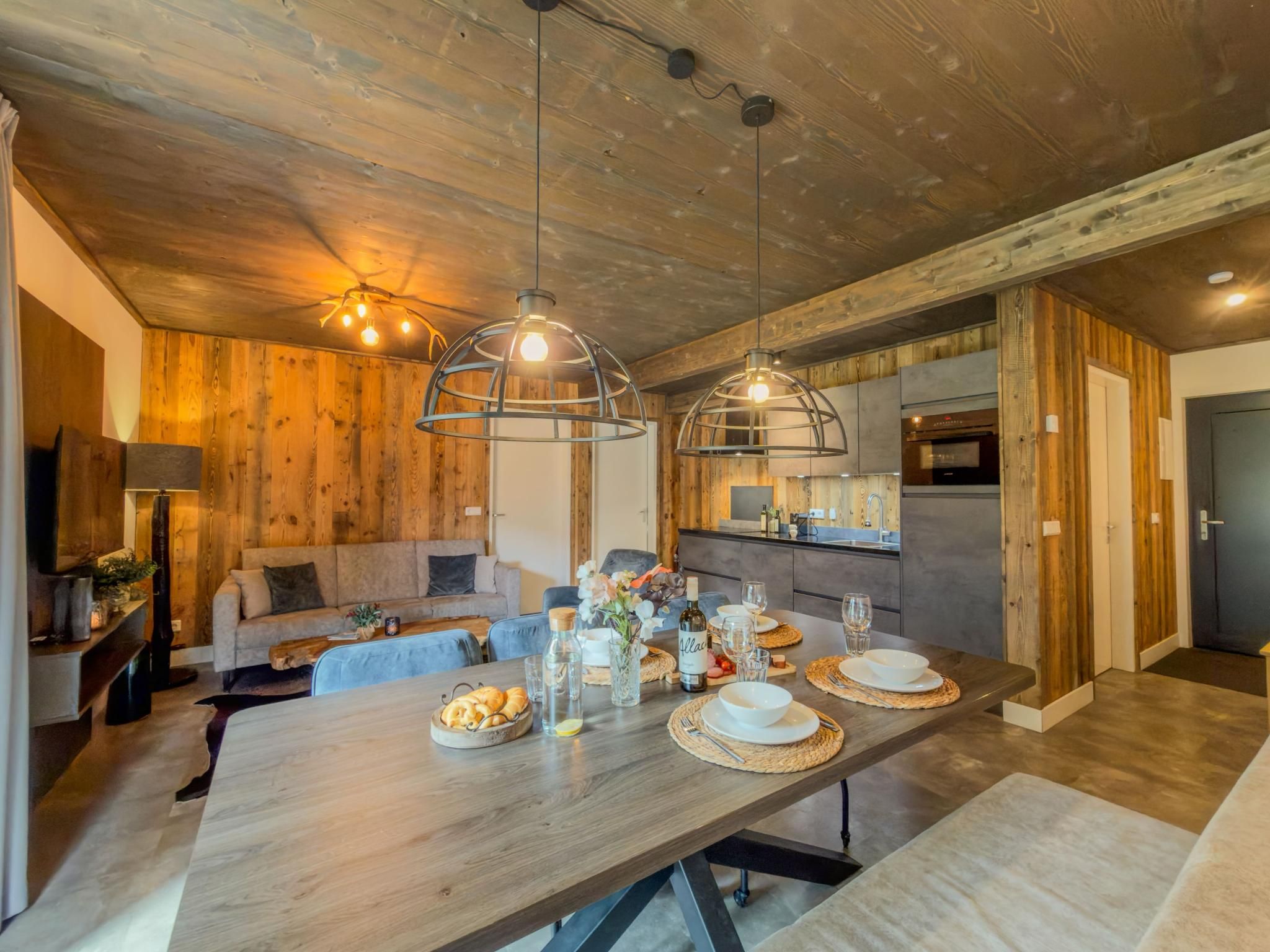 Een moderne eethoek met een houten tafel gedekt voor een maaltijd, een bank en een keuken op de achtergrond.
