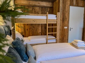 Une pièce en bois aménagée comme une cabine, avec des lits superposés, une échelle, une porte et une pile de serviettes.