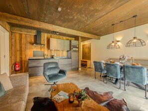 Eine moderne Küche mit Holzakzenten, ein Essbereich mit blauen Stühlen und eine gemütliche Sitzecke mit einer Ledersofa und einem Holztisch.