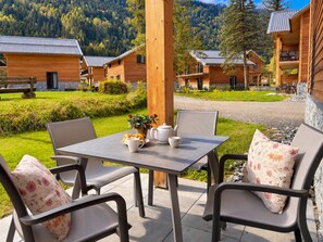 Eine Holzhütte mit einer Terrassentisch und -stühlen, umgeben von einem üppigen Garten und einem Bergpanorama.