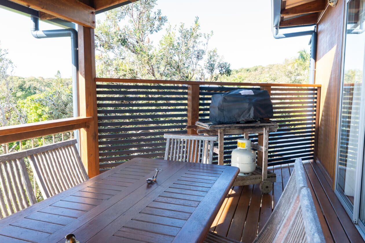 A wooden deck with a table and grill, surrounded by a wooden fence, overlooking a natural landscape.