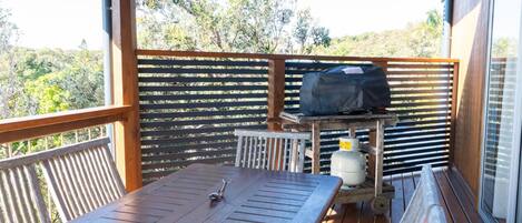 A wooden deck with a table and grill, surrounded by a wooden fence, overlooking a natural landscape.