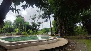 Une piscine circulaire bordée de béton, entourée d’une zone de gravier et d’arbres.