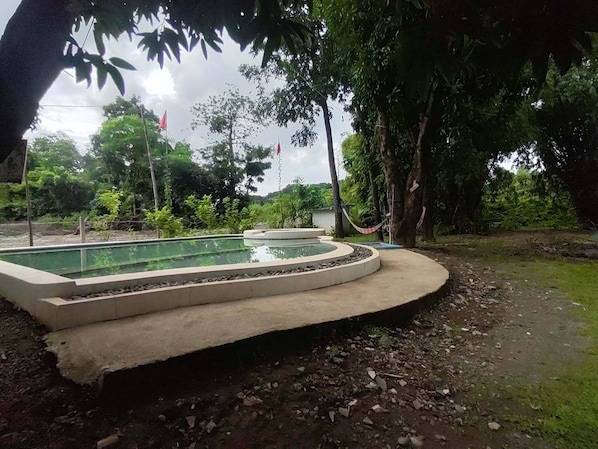 Una piscina circular con borde de hormigón, rodeada de grava y árboles.