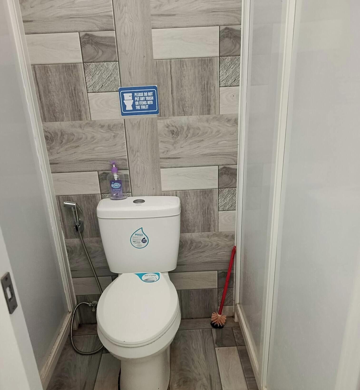 Et badeværelse med toilet, sæbedispenser og et skilt, der instruerer om ikke at smide affald i toilettet.