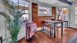 A room with a wooden floor, a table with chairs, a bench, a potted plant, and a window with blinds. - Boho Serenity on the Southside- Workspace/Patio (Birmingham)