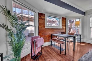 A room with a wooden floor, a table with chairs, a bench, a potted plant, and a window with blinds. - Boho Serenity on the Southside- Workspace/Patio (Birmingham)