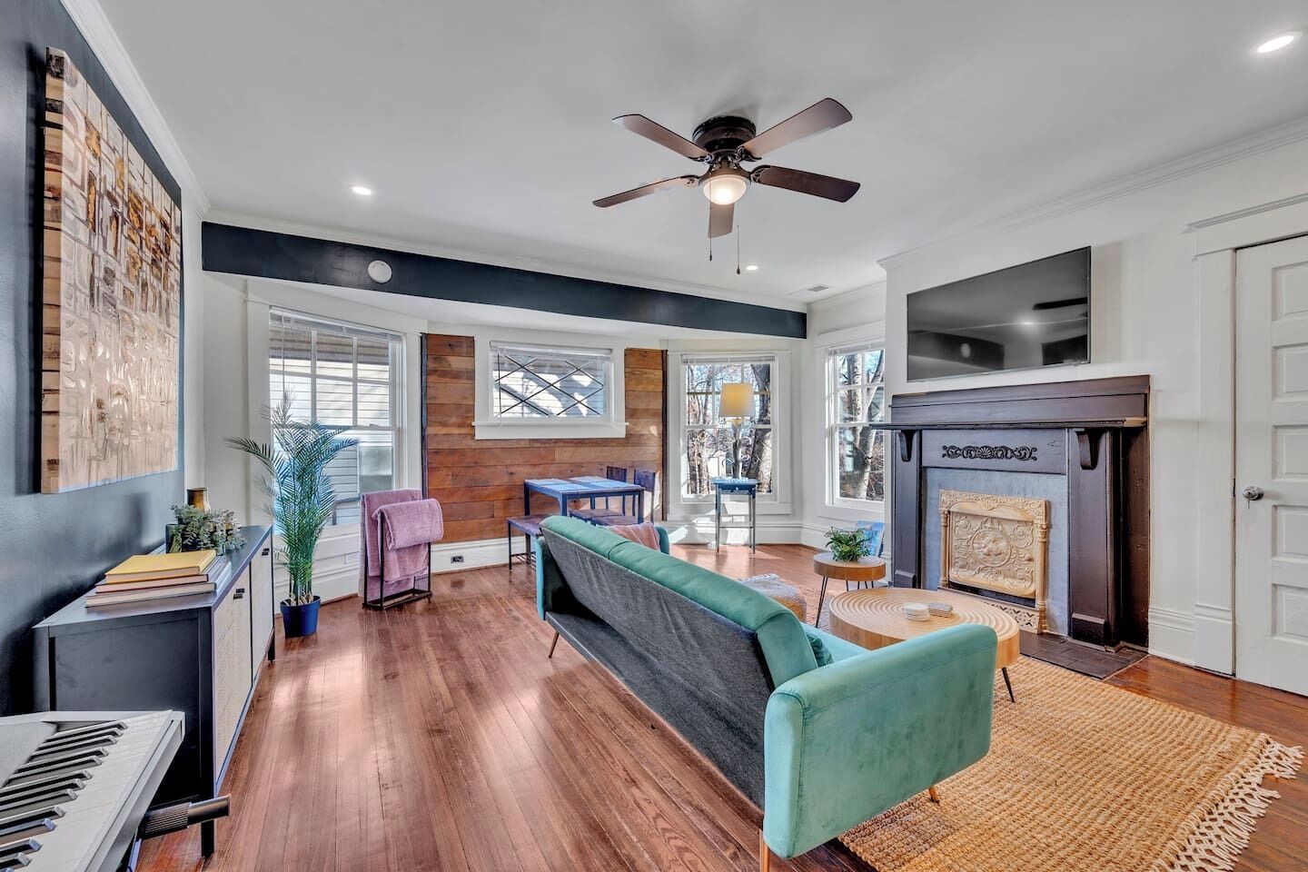 A spacious living room with hardwood flooring, a teal sofa, a fireplace, and a ceiling fan.