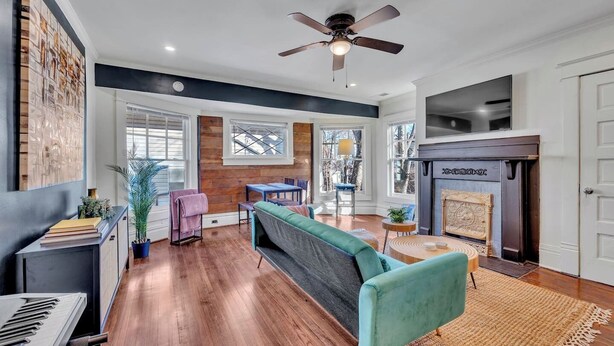 A spacious living room with hardwood flooring, a teal sofa, a fireplace, and a ceiling fan. - Boho Serenity on the Southside- Workspace/Patio (Birmingham)