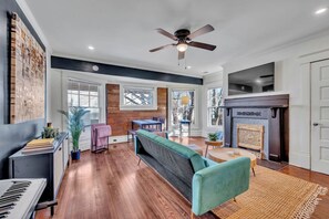 A spacious living room with hardwood flooring, a teal sofa, a fireplace, and a ceiling fan. - Boho Serenity on the Southside- Workspace/Patio (Birmingham)