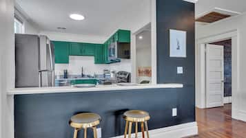 A modern kitchen with teal cabinets, a stainless steel refrigerator, and a bar area with stools.