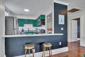 A modern kitchen with teal cabinets, a stainless steel refrigerator, and a bar area with stools. - Boho Serenity on the Southside- Workspace/Patio (Birmingham)