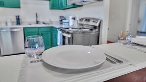 A dining table set with a plate, cutlery, and two glasses, with a kitchen in the background. - Boho Serenity on the Southside- Workspace/Patio (Birmingham)