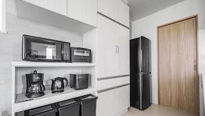 Una cocina moderna con armarios blancos, un refrigerador negro, un microondas, una cafetera y un hervidor.