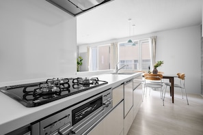 A modern kitchen with a gas stove, a built-in oven, and a dining area with a table and chairs. - R&r Asahikawa (Asahikawashi)