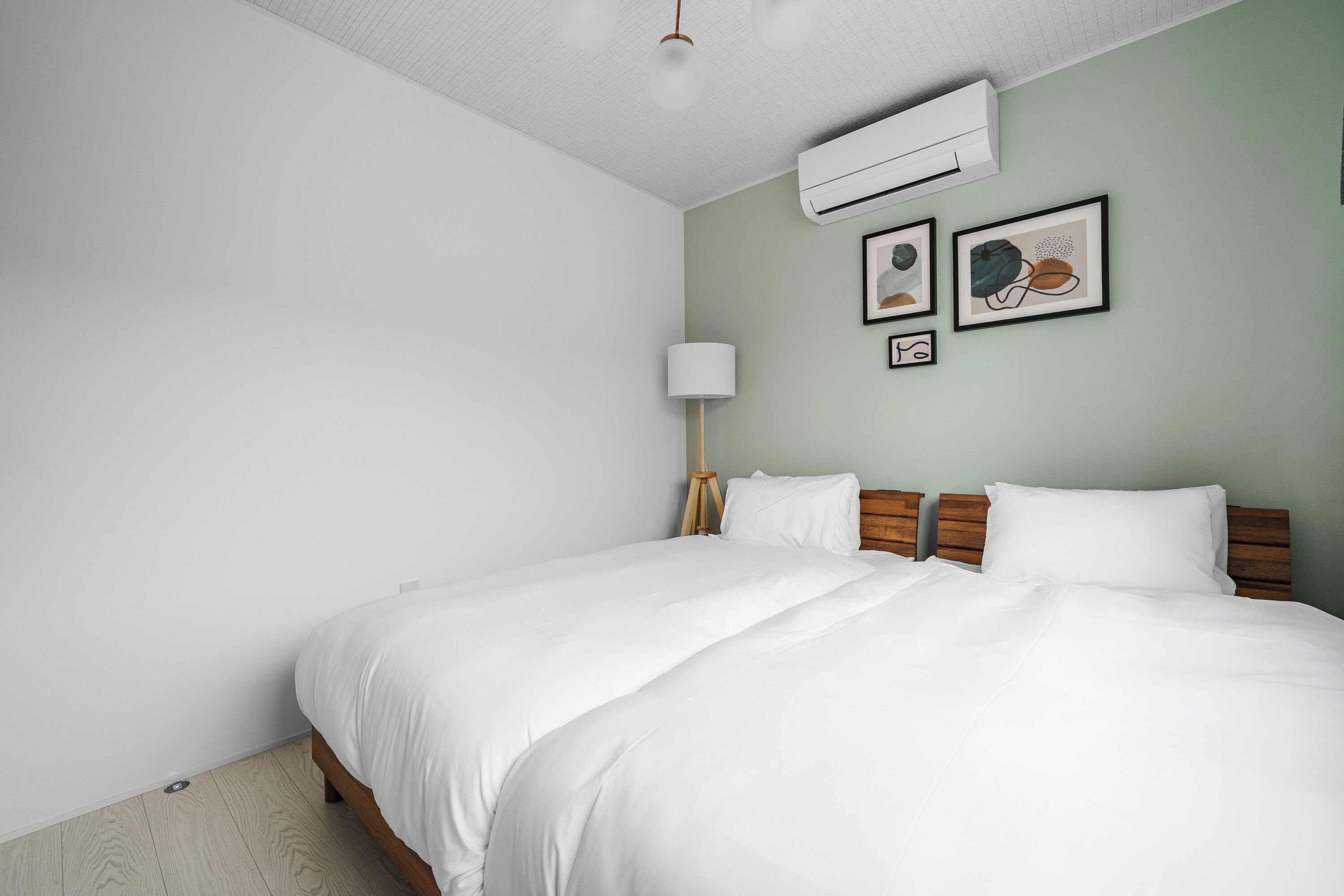 A bedroom with a bed, a wall-mounted air conditioner, and two framed pictures.