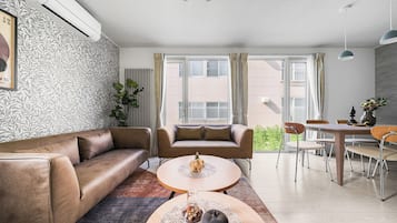A modern living room with a sofa, a coffee table, and a dining area with chairs and a table.