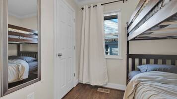 A bedroom with bunk beds, a window with curtains, a door, and a mirror.