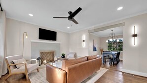 Een moderne woonkamer met een bank, een stoel, een open haard en een eethoek met een tafel en stoelen.
